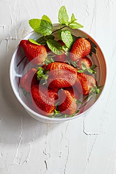 Bowl with delicious large strawberries fresones, fresh, whole, freshly cut and with peppermint. On delicate white textured