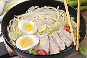 Bowl of delicious rice noodle soup with meat and egg on wooden board, closeup