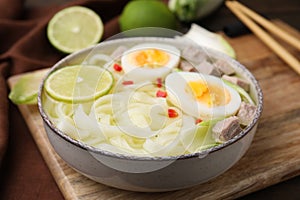 Bowl of delicious rice noodle soup with meat and egg on wooden board, closeup