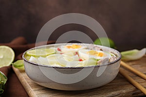 Bowl of delicious rice noodle soup with meat and egg on wooden board, closeup