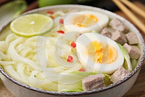 Bowl of delicious rice noodle soup with meat and egg on wooden board, closeup