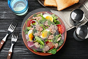 Bowl of delicious salad with canned tuna and vegetables served on black wooden table, flat lay