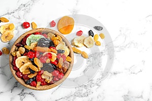 Bowl of different dried fruits on marble background, top view with space for text