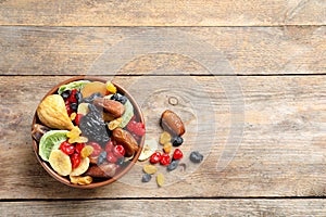 Bowl of different dried fruits on wooden background, top view with space for text