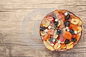 Bowl with different tasty dried fruits on wooden table, top view. Space for text