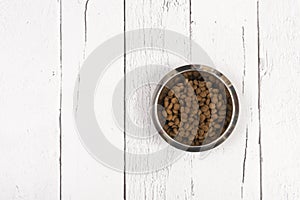 Bowl with dog kibble on white wooden planks