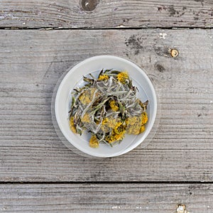 bowl with dried coltsfoot on a wooden background