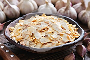Bowl of dried garlic flakes, garlic cloves. Heads of garlic on background.