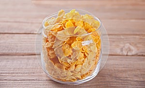 A bowl of dry corn flakes cereal on wooden background