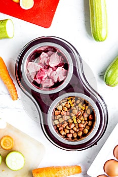 Bowl of dry dogfood, carrot, courgette and meat table background