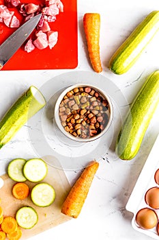 Bowl of dry dogfood, carrot, courgette and meat table background top view photo