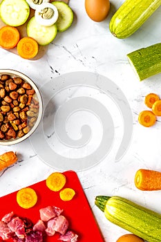 Bowl of dry dogfood, carrot, courgette, meat table background top view mock-up photo