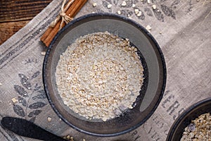 A bowl with dry flakes of oatmeal. Still life on textiles and wooden background.