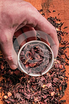 A bowl of dry hibiscus in a small bowl, male hand. A healthy herb for healthy life.