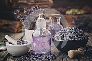 Bowl of dry lavender flowers, mortars, bottles of essential lavender oil or infused water. Old books and medicinal herbs on