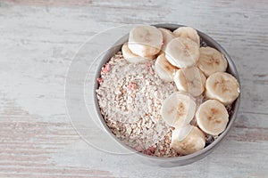 Bowl of dry oat flakes oatmeal with dry berries and sliced banana on wooden table.