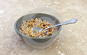 Bowl of dry organic breakfast cereal with dried blueberries and pumpkin seeds plus a spoon in the food