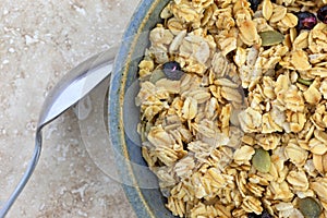 Bowl of dry organic breakfast cereal with dried blueberries and pumpkin seeds plus a spoon to the side