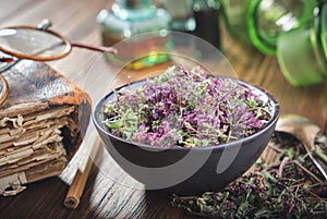 Bowl of dry Origanum vulgare or wild marjoram flowers, old book and bottles of essential oil.