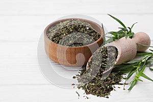 Bowl of dry tarragon, scoop and fresh leaves on white wooden table