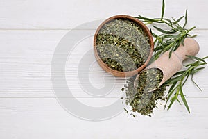 Bowl of dry tarragon, scoop and fresh leaves on white wooden table, flat lay. Space for text