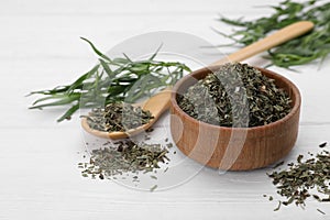 Bowl of dry tarragon, spoon and fresh leaves on white wooden table