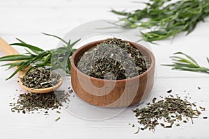 Bowl of dry tarragon, spoon and fresh leaves on white wooden table