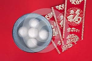 A bowl of dumplings and red envelopes on a red background.The Chinese meaning in the picture is `happiness` and `good luck`