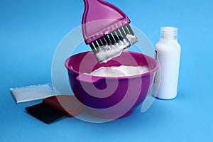 Bowl with dye and hair coloring kit on a blue background