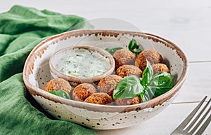 Bowl of falafel with tzatziki sauce on a white wooden table