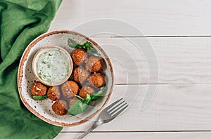Bowl of falafel with tzatziki sauce on a white wooden table