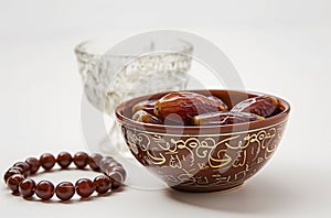 a bowl of dates, a prayer beads, a glass and a copy of the Holy Quran over white background