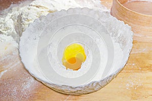 Bowl with flour and broken egg on the table