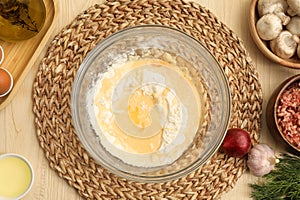 Bowl with flour, eggs and products on wooden table, flat lay