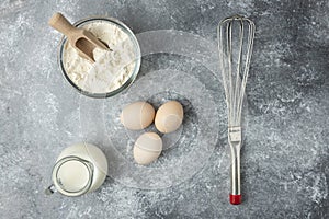 Bowl of flour, eggs and whisker on marble surface