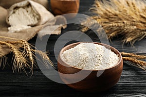 Bowl of flour and wheat ears on black wooden table