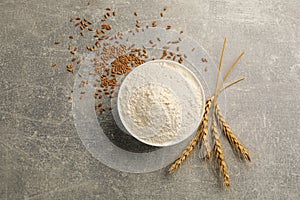 Bowl of flour, wheat ears and kernels on light grey table, flat lay