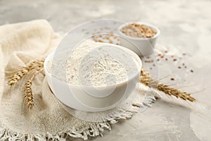 Bowl of flour and wheat ears on light grey table