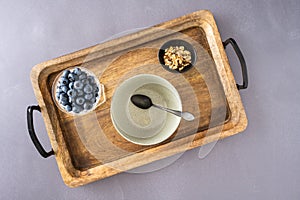 Bowl of fresh blueberries, small bowl of walnuts, and empty bowl with spoon on a rustic wooden serving tray