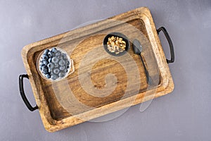Bowl of fresh blueberries, small bowl of walnuts, and a spoon on a rustic wooden serving tray