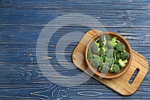 Bowl of fresh broccli on blue wooden table, top view with space for text