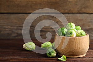Bowl with fresh Brussels sprouts on brown wooden table, closeup. Space for text