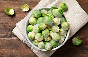 Bowl of fresh Brussels sprouts and napkin on wooden background, top vie