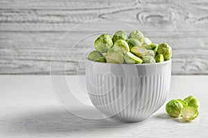 Bowl of fresh Brussels sprouts on table against wooden background.