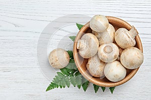 Bowl of fresh champignon mushrooms on wooden background, top view