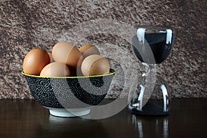 Bowl of Fresh Eggs with Sand Glass Timer on a Polished Wooden Surface with Mottled Background