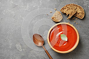 Bowl of fresh homemade tomato soup and bread on grey background, top view.