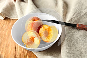 Bowl with fresh peaches and knife on wooden table