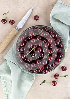 Bowl of fresh red cherries and knife on beige background. Top view