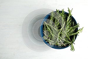 Bowl with fresh rosemary twigs on wooden table, top view.